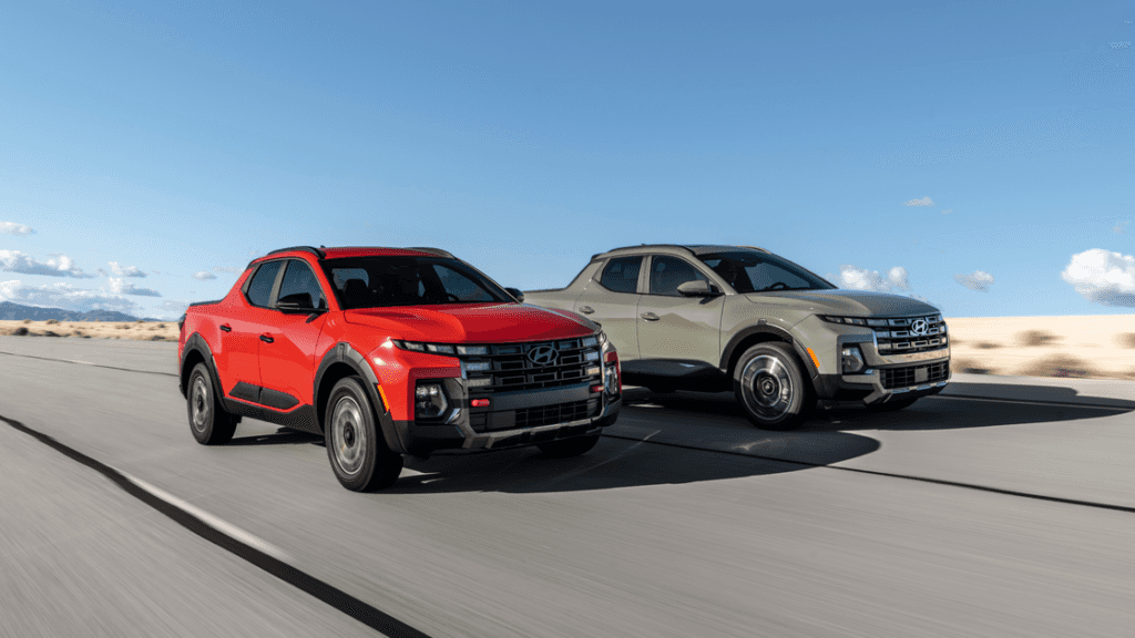 2026 Hyundai Santa Cruz in red and sage green driving side by side on an open highway, emphasizing bold pickup styling with updated grille and LED lighting.