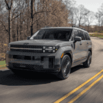 Gray 2026 Hyundai Santa Fe SUV driving on a winding forest road, featuring boxy front fascia, blacked-out grille, and LED headlights.