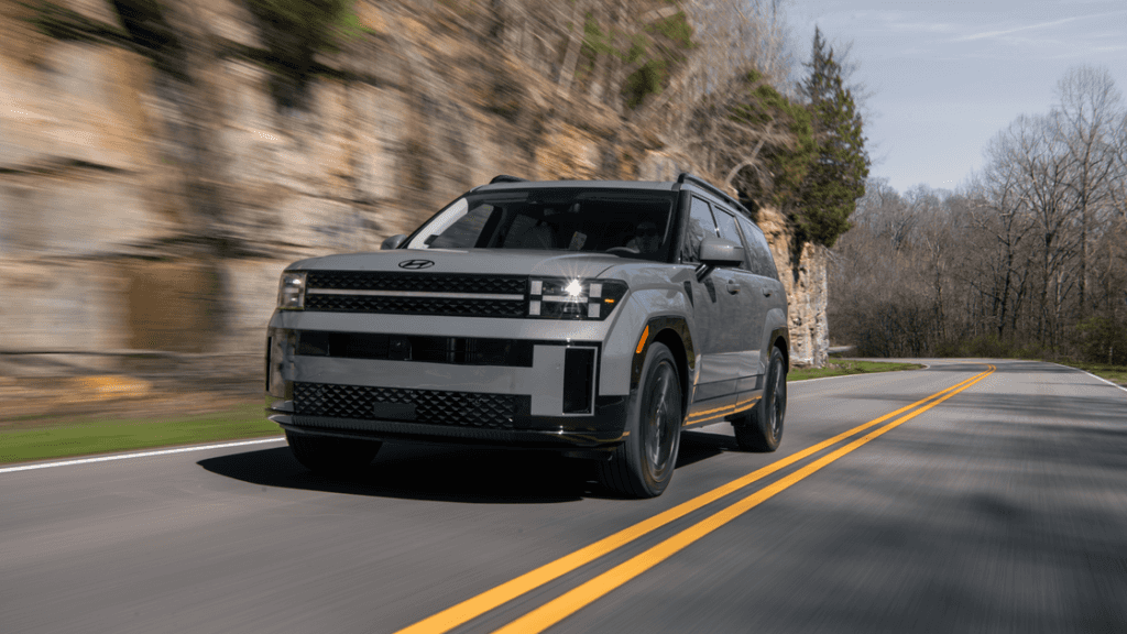 2026 Hyundai Santa Fe in matte gray driving on scenic road with LED headlights and bold grille.