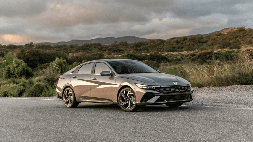 2025 Hyundai Elantra exterior side angle in metallic gray parked on scenic road with greenery.