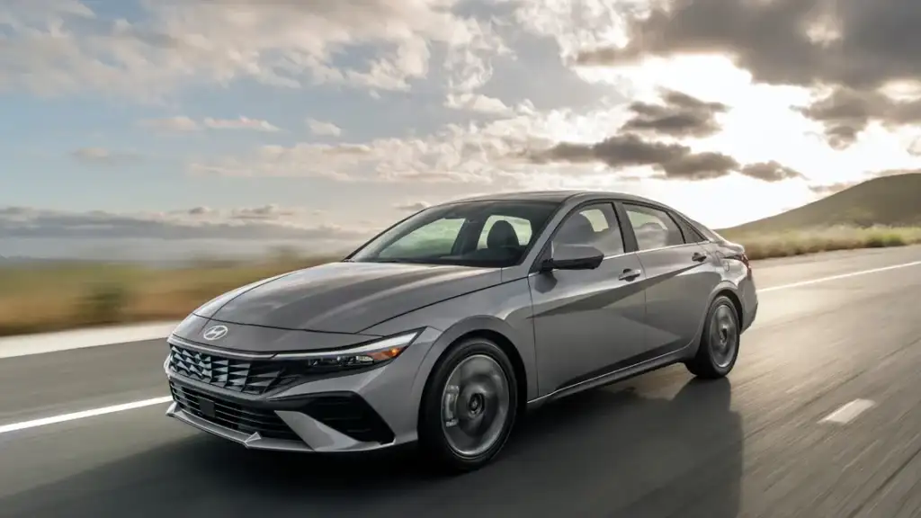 2026 Hyundai Elantra sedan in metallic gray driving on open road with cloudy sky backdrop.