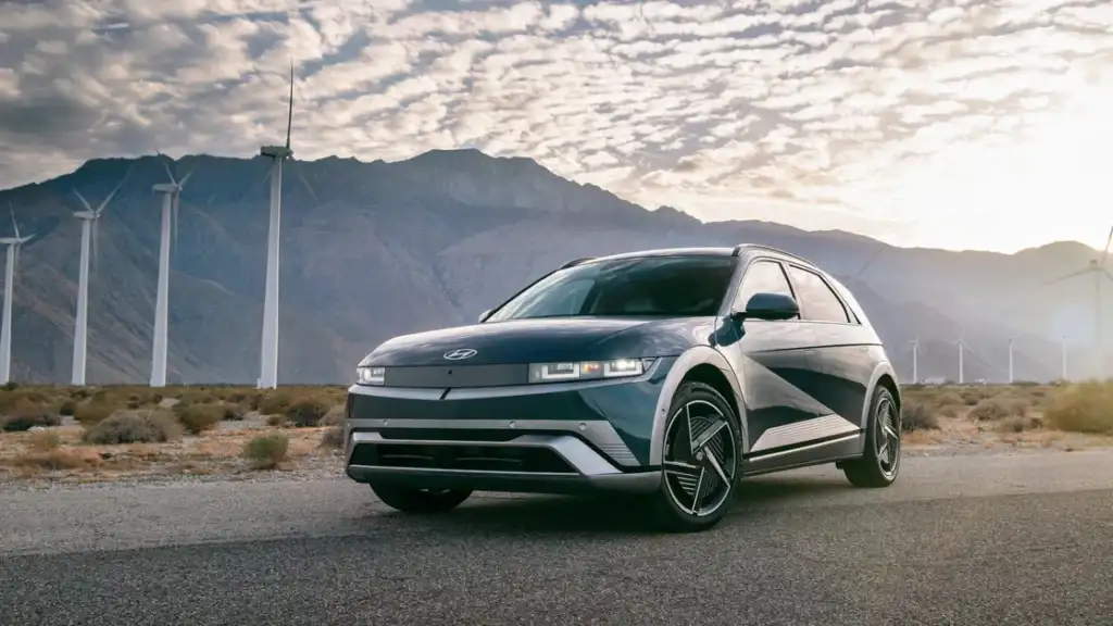 2026 Hyundai IONIQ 5 electric SUV parked near wind turbines with mountain scenery in background.