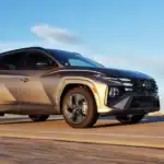 2026 Hyundai Tucson SUV in bronze finish driving on highway with clear sky and sunlight view.