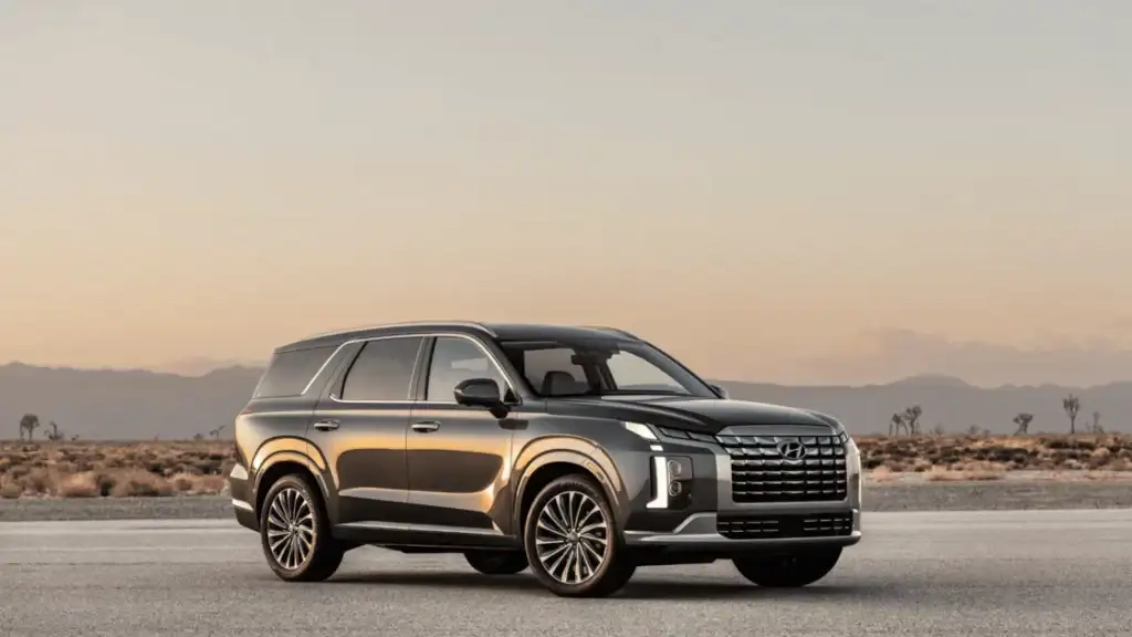 Front-side view of the 2025 Hyundai Palisade SUV in dark gray, parked on desert pavement at sunset.