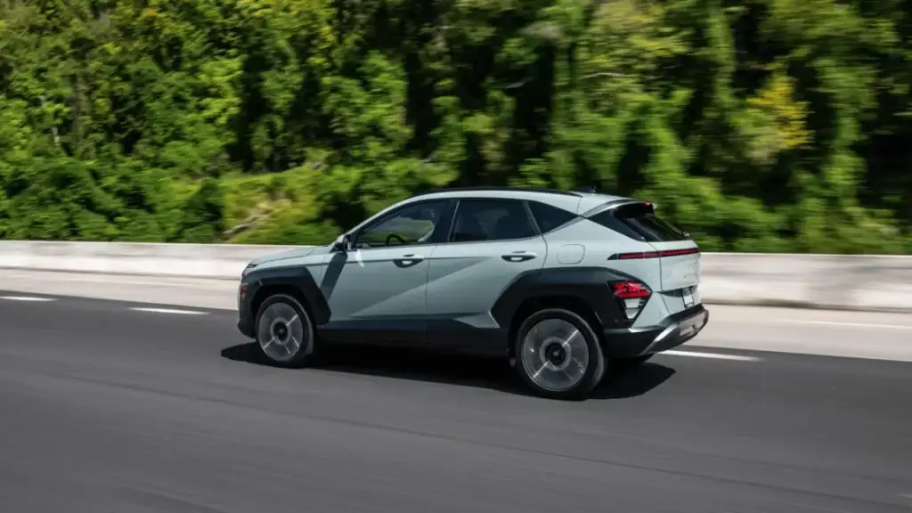 Light green 2026 Hyundai Kona compact SUV driving on a forest highway, showcasing aerodynamic side profile.