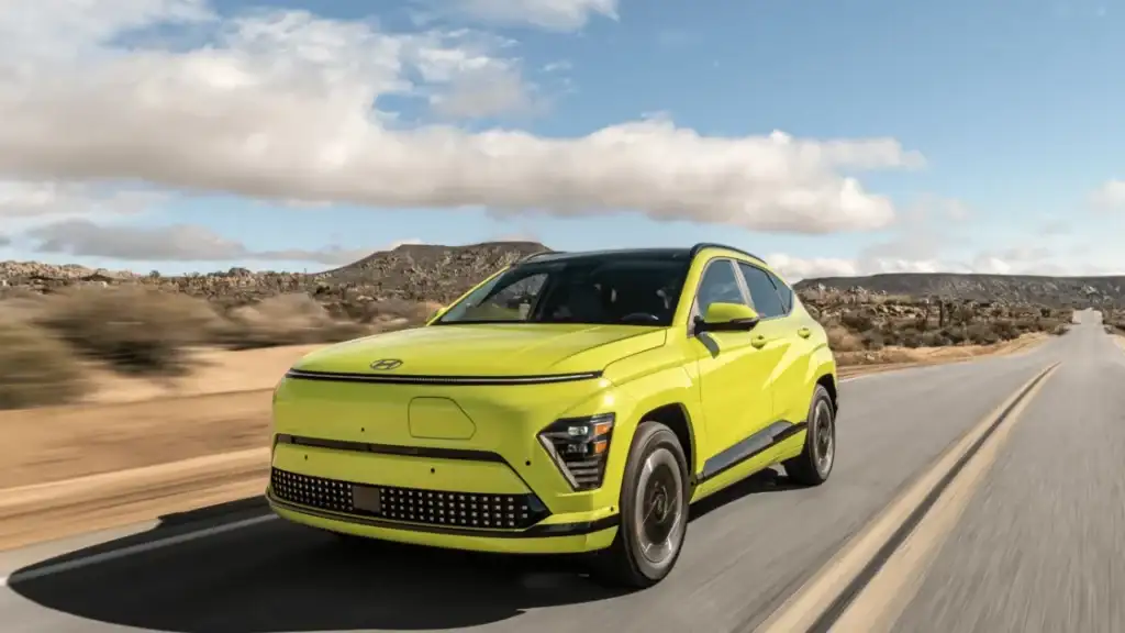 Vibrant yellow 2026 Hyundai Kona Electric crossover driving through a desert highway under bright daylight.