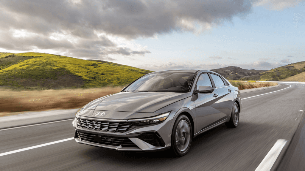 2025 Hyundai Elantra driving on an open highway with rolling green hills under cloudy skies.