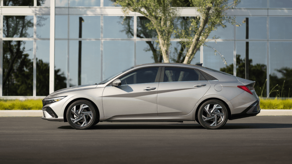 2025 Hyundai Elantra side profile in silver parked by modern glass building under sunlight.