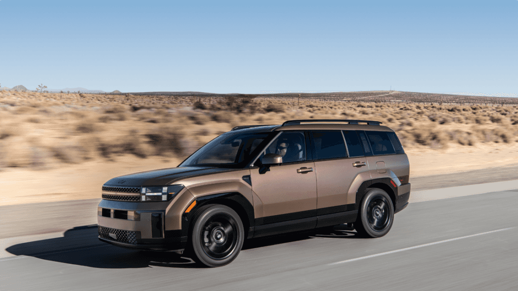 2025 Hyundai Santa Fe Hybrid cruising on a desert road with clear blue skies and rocky terrain ahead.