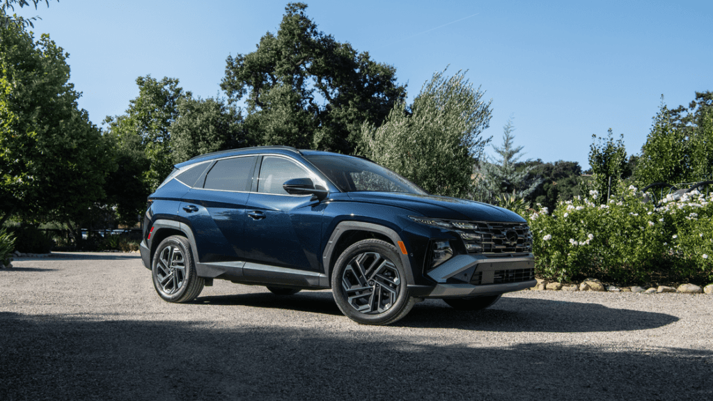 2025 Hyundai Tucson Hybrid blue SUV parked on gravel with trees and greenery behind.