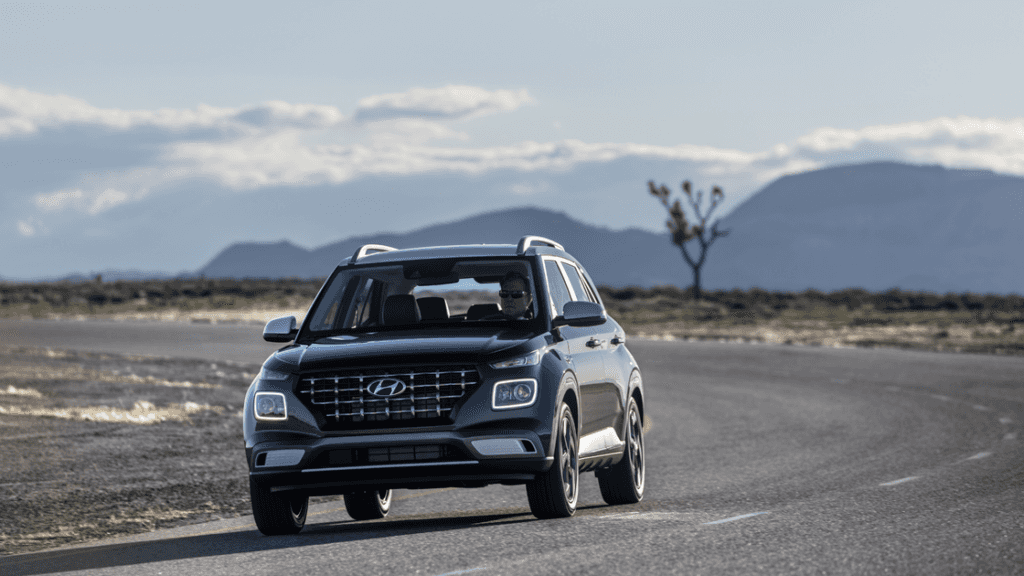 2025 Hyundai Venue driving on a winding desert road with mountain landscape and open sky behind.