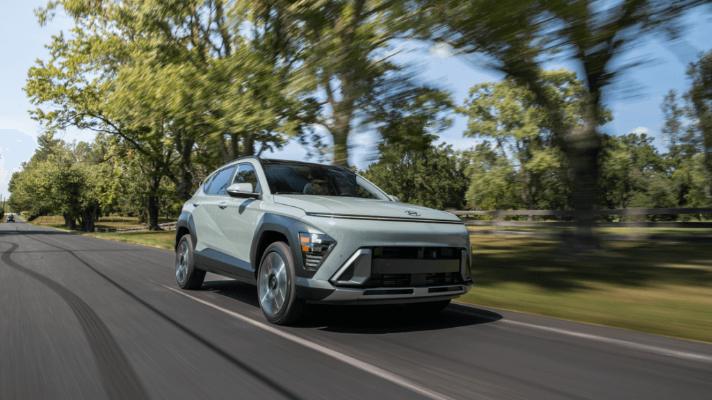 2026 Hyundai Kona compact SUV driving through tree-lined road showcasing bold front design.