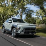 2026 Hyundai Kona compact SUV driving through tree-lined road showcasing bold front design.