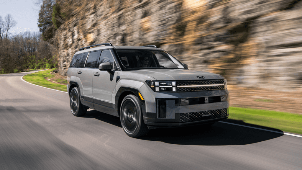 2026 Hyundai Santa Fe SUV driving on scenic road featuring boxy design and modern lighting.