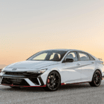 2026 Hyundai Elantra N sport sedan front three quarter view in white driving at sunset.