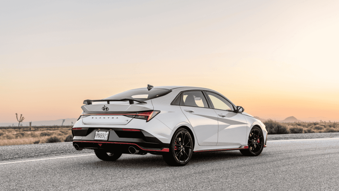 Rear three quarter view of the 2026 Hyundai Elantra N showing sporty design, black wheels, rear spoiler, and aggressive performance styling.