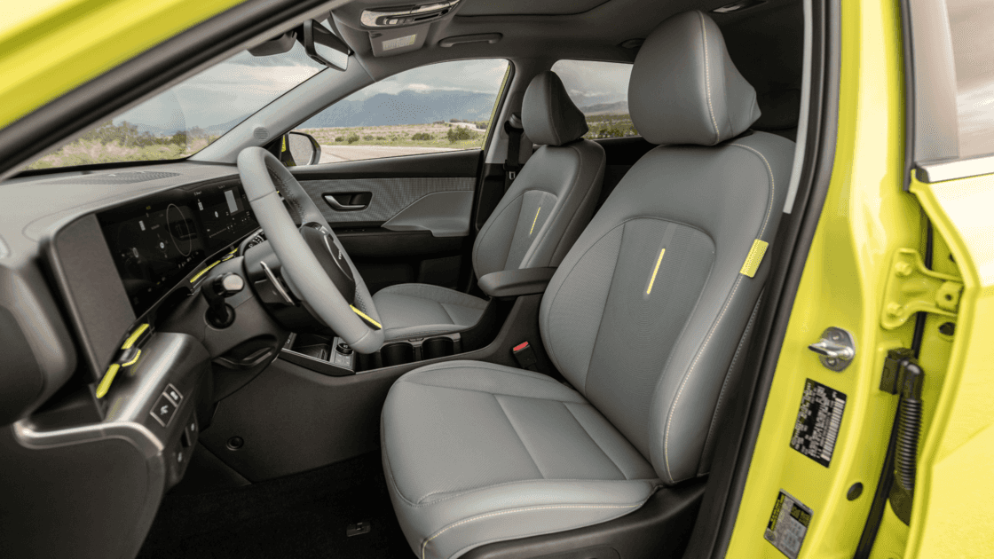 Front interior seating view of the 2026 Hyundai Kona Electric showing gray seats, yellow accents, and spacious electric SUV cabin.