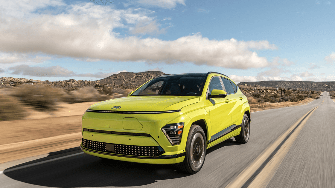 2026 Hyundai Kona Electric SUV front three quarter view in green driving on desert highway.