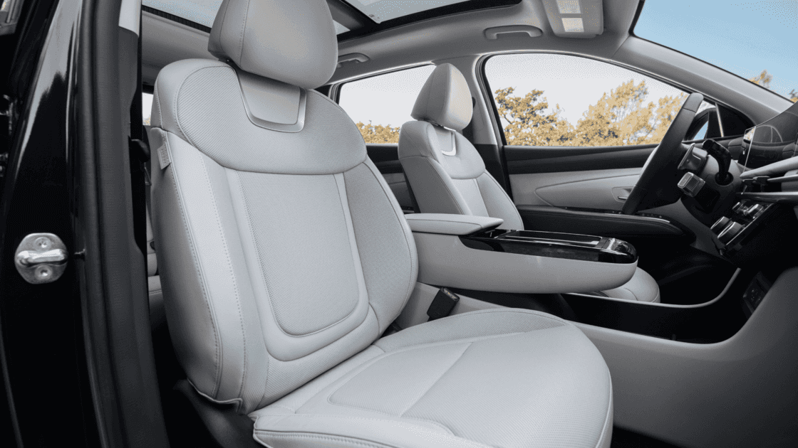Front interior seating view of the 2026 Hyundai Tucson Hybrid showcasing light upholstery, center console, and driver focused layout.