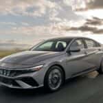 2026 Hyundai Elantra sedan driving on an open highway, showing sleek exterior styling and aerodynamic front design.