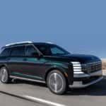 2026 Hyundai Palisade SUV driving on a rural road, showcasing bold grille design, LED lighting, and spacious profile.