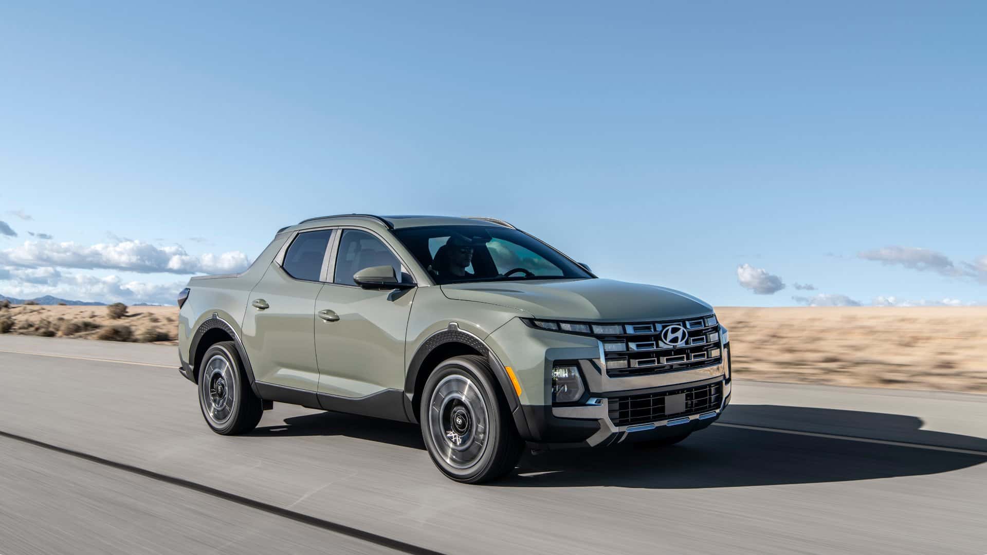 2026 Hyundai Santa Cruz sport adventure truck driving on an open road, highlighting compact pickup design, bold grille, and rugged stance.