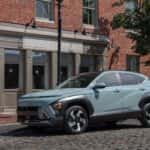 2026 Hyundai Kona compact SUV front three quarter view parked on city street highlighting updated exterior styling and LED daytime running lights.