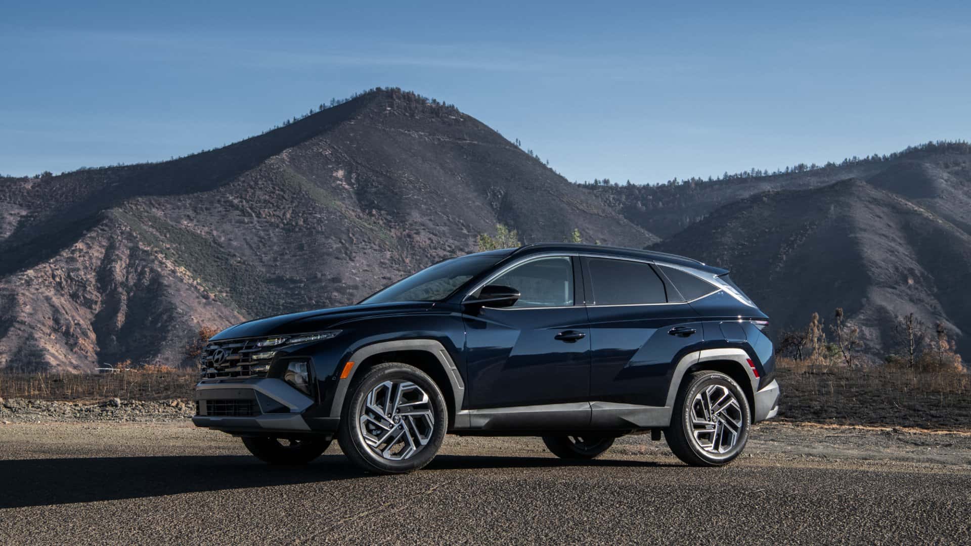 2026 Hyundai Tucson Hybrid SUV side profile in mountainous landscape showcasing hybrid capability rugged styling and alloy wheels.