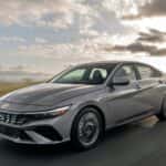 2026 Hyundai Elantra sedan driving on an open road in front three quarter view.