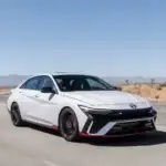 2026 Hyundai Elantra N white sport sedan driving on desert road with black wheels and red trim.