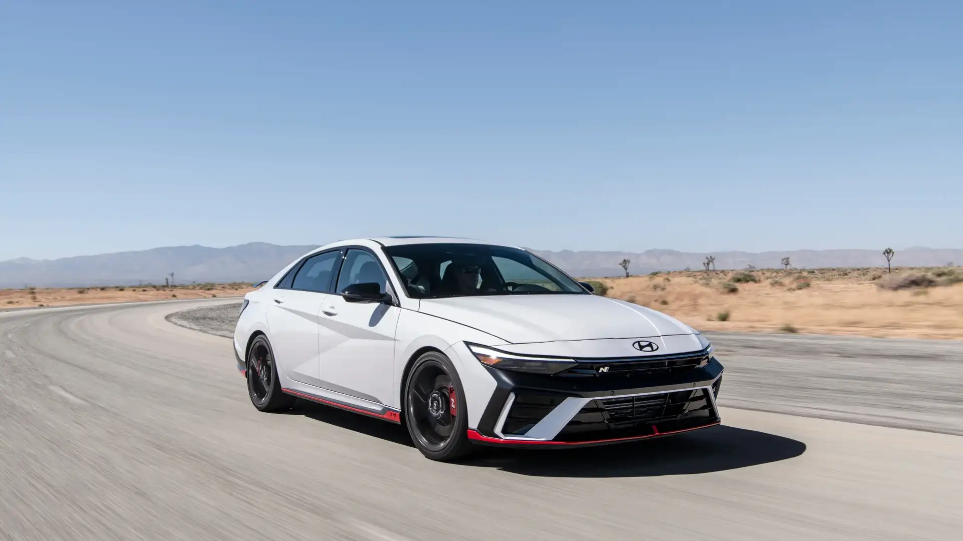 2026 Hyundai Elantra N white sport sedan driving on desert road with black wheels and red trim.