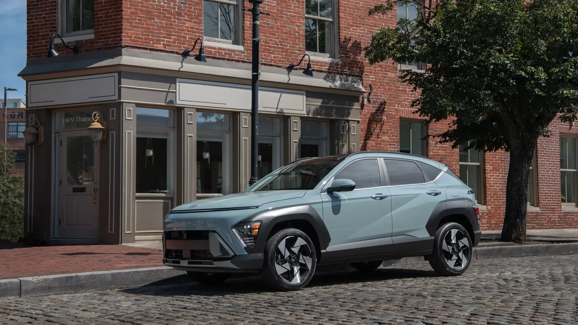 2026 Hyundai Kona green compact SUV parked on cobblestone street near brick building.