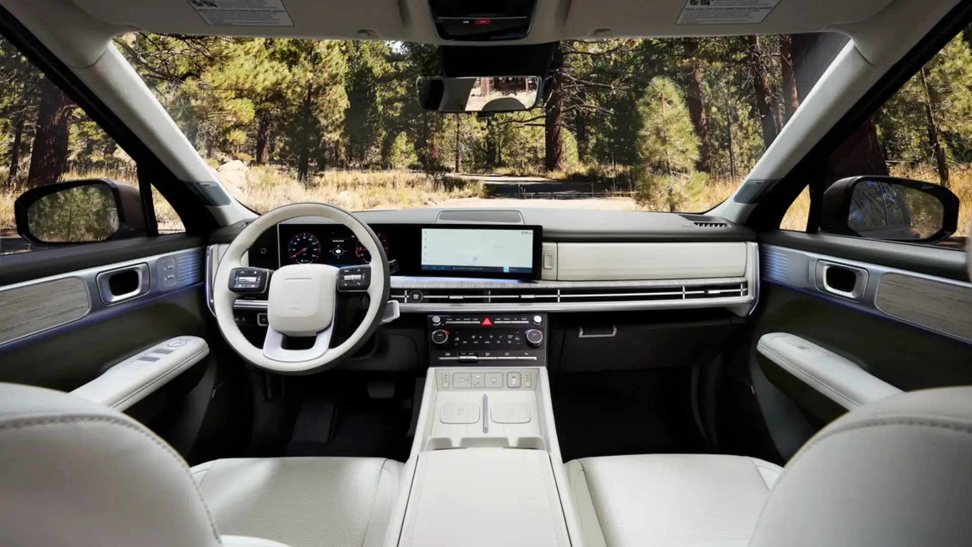 2026 Hyundai Santa Fe Hybrid dashboard with wide touchscreen, light interior trim, and forest road view.