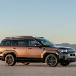 2026 Hyundai Santa Fe Hybrid brown SUV shown in side profile on desert road with mountain backdrop.