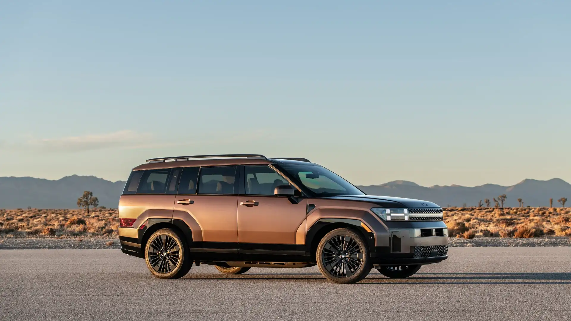2026 Hyundai Santa Fe Hybrid brown SUV shown in side profile on desert road with mountain backdrop.