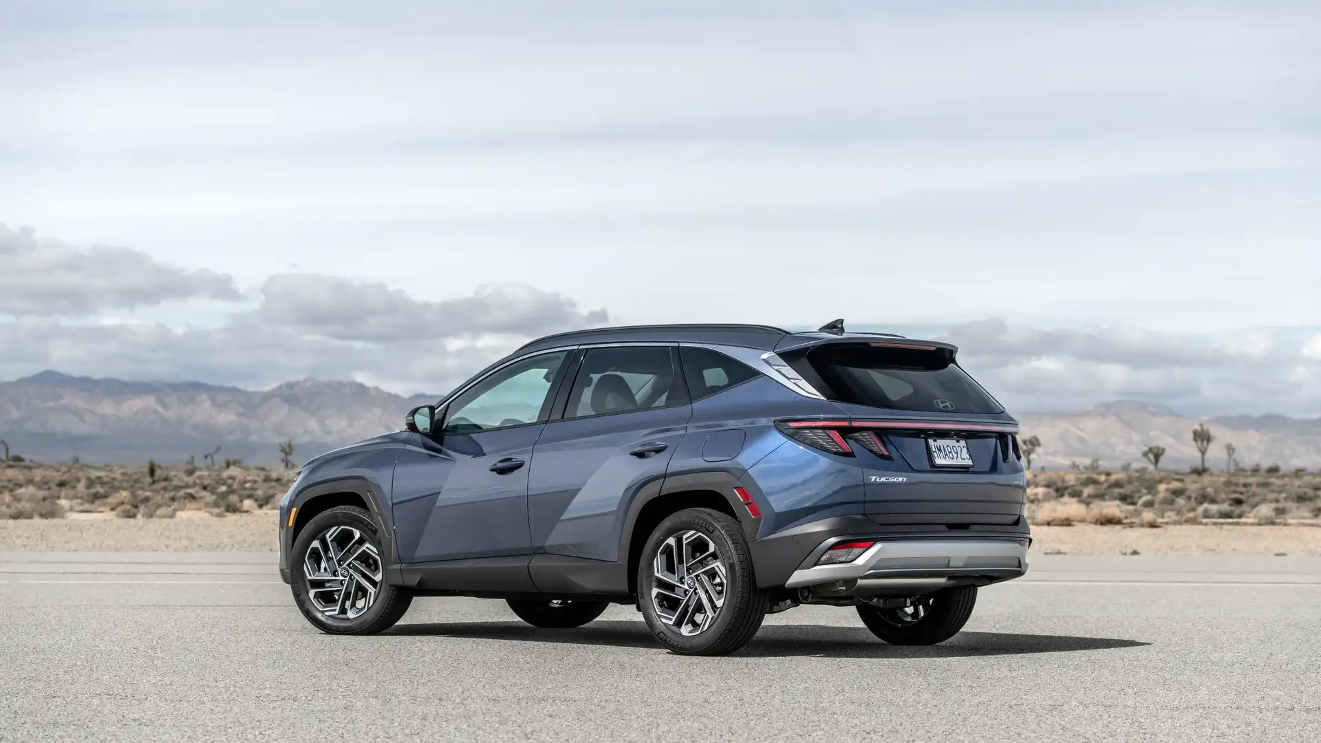 2026 Hyundai Tucson blue SUV shown from rear angle in desert landscape with angular body styling.
