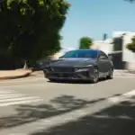 2026 Hyundai Elantra gray sedan driving through city street with sleek front grille and motion blur.