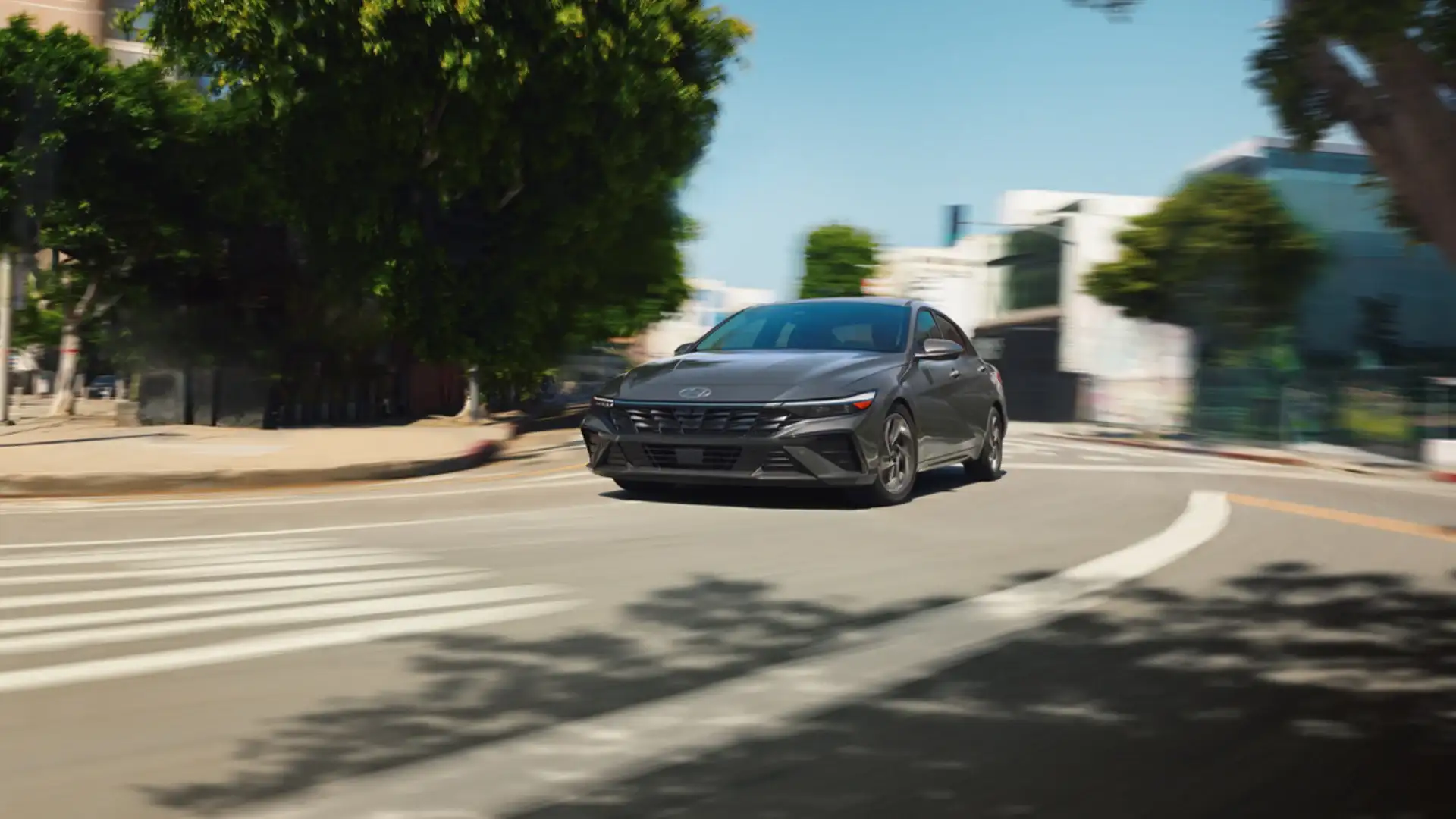 2026 Hyundai Elantra gray sedan driving through city street with sleek front grille and motion blur.