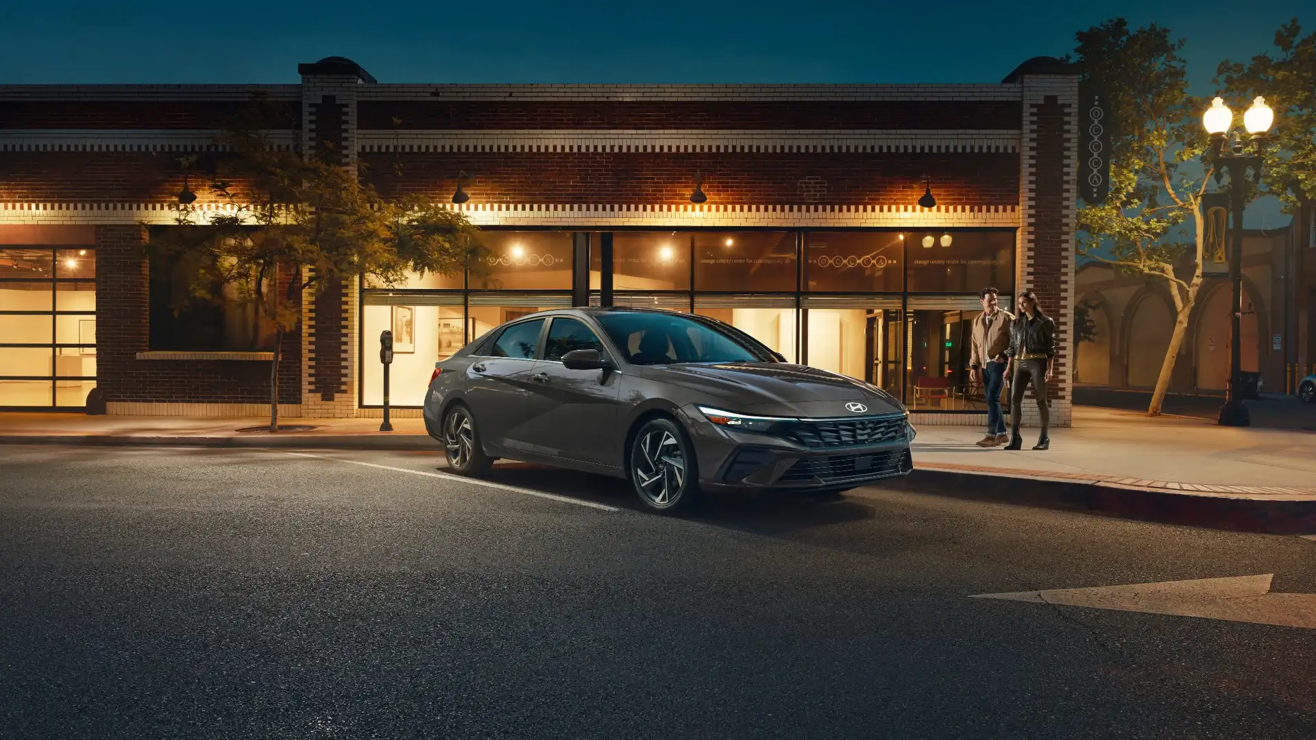 2026 Hyundai Elantra gray sedan parked at night outside a brick building with LED headlights.