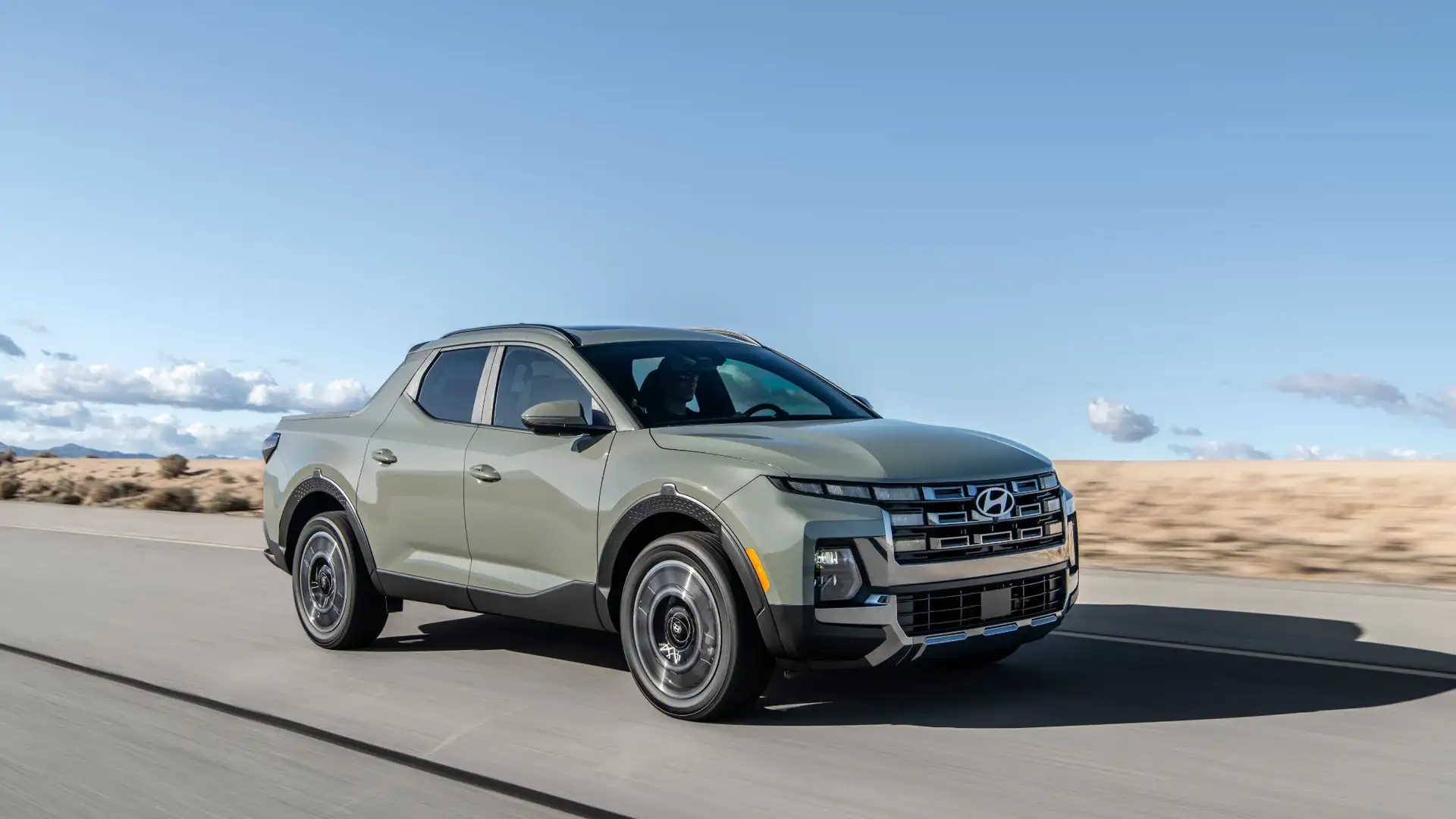 2026 Hyundai Santa Cruz compact pickup driving on highway with desert landscape background.