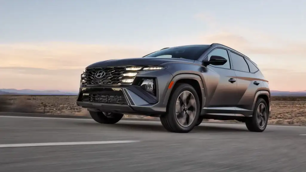 2026 Hyundai Tucson Hybrid gray SUV driving on open road at sunset with LED headlights.