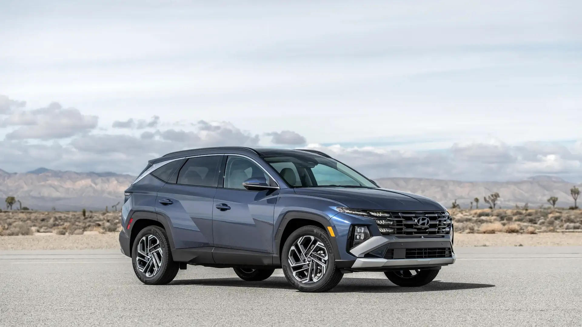 2026 Hyundai Tucson Hybrid blue SUV parked in desert setting with modern grille and alloy wheels.