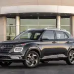 2026 Hyundai Venue gray compact SUV parked outside modern building with front grille and roof rails.