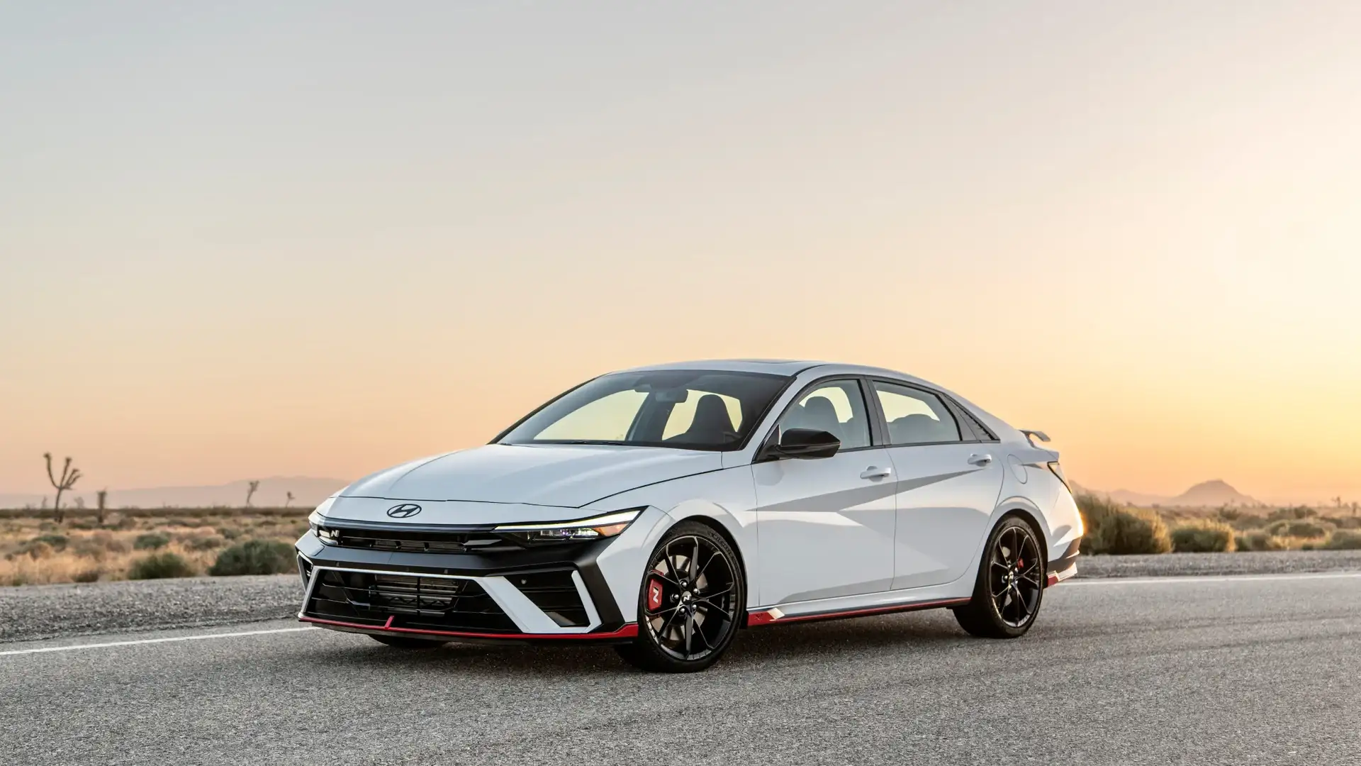 2026 Hyundai Elantra N white sport sedan parked on desert road at sunset with black wheels and red trim.