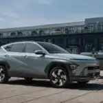 2026 Hyundai Kona green compact SUV parked by waterfront buildings with side profile and angular styling.