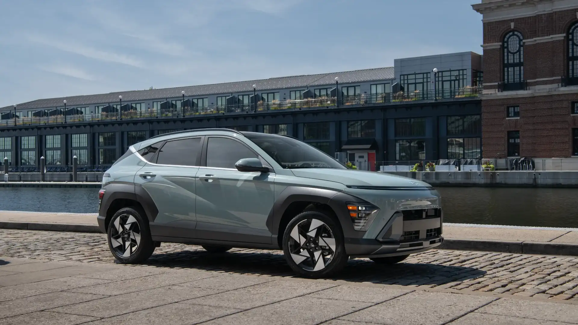 2026 Hyundai Kona green compact SUV parked by waterfront buildings with side profile and angular styling.