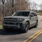 2026 Hyundai Santa Fe gray SUV driving on wooded road with boxy body design and black wheels.