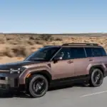 2026 Hyundai Santa Fe Hybrid bronze SUV driving on desert highway with roof rails and black wheels.