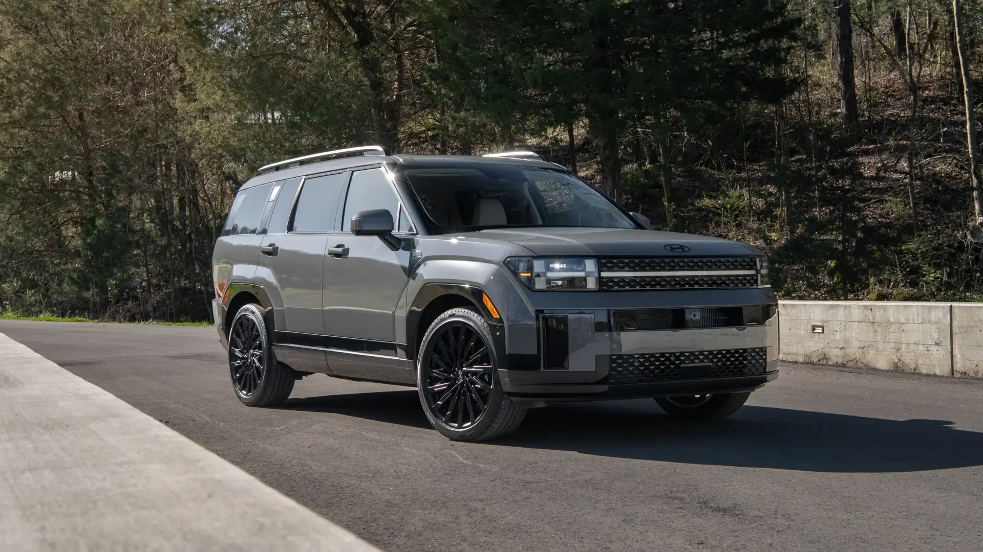 2026 Hyundai Santa Fe gray SUV parked near wooded road with boxy body design and black wheels.