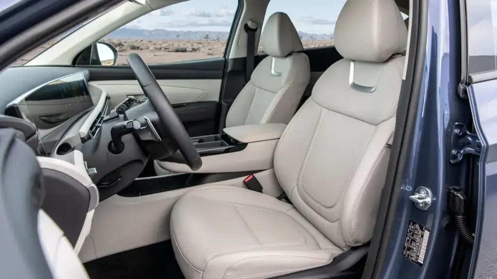 2026 Hyundai Tucson interior with light front seats, digital display, and open driver door view.